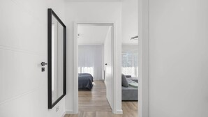 A modern hallway with a framed picture on the left, leading to a bedroom with a bed and a gray sofa in the background. - Stylish Apartment with Terrace | Spa Access and Parking (Dziwnów)