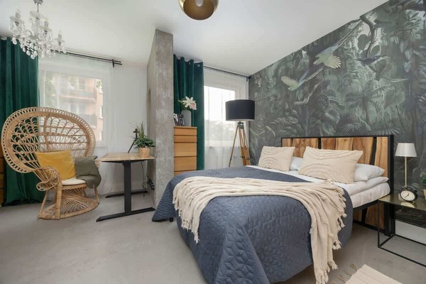 A cozy bedroom with designer wallpaper, a wicker chair, and modern lighting invites you to relax after a full day of exploring.