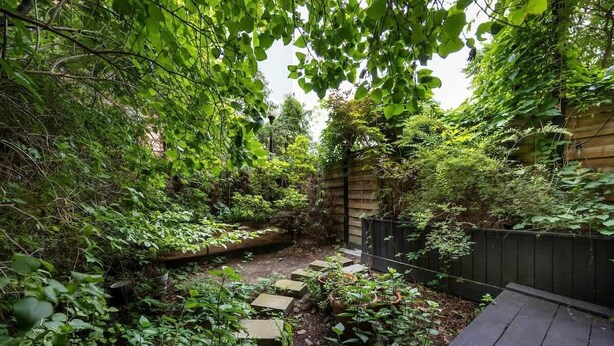 Um jardim com deck de madeira, degraus de pedra e folhagem densa.