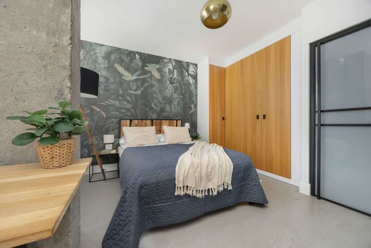 Ein Schlafzimmer mit einem Bett, einem Holzschrank, einer Betonwand und einem großen Fenster.