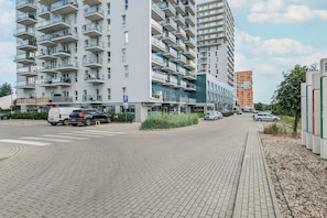 A multi-story residential building with balconies, a parking area, and a pedestrian walkway.
