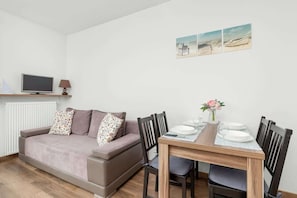 A room with a sofa, a TV, a dining table with chairs, and a radiator.