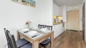 A dining area with a wooden table set for four, white chairs, and a vase with pink flowers. There are three framed pictures on the wall above the table.