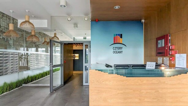 A modern reception area with a wooden reception desk, a glass partition, and a wall-mounted logo for 'Cztery Oceany'.