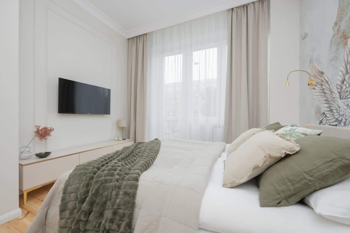 Ein modernes Schlafzimmer mit Bett, Flachbildfernseher, Nachttisch und einem Fenster mit Vorhängen.