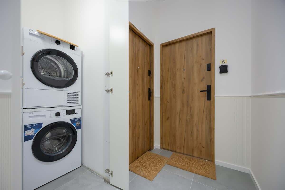 A laundry room with stacked washing machines, a wooden door, and a small mat at the entrance.