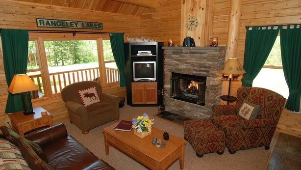 Interior acogedor de una cabaña con chimenea, paredes de madera y un letrero que dice 'RANGELEY LAKES'.