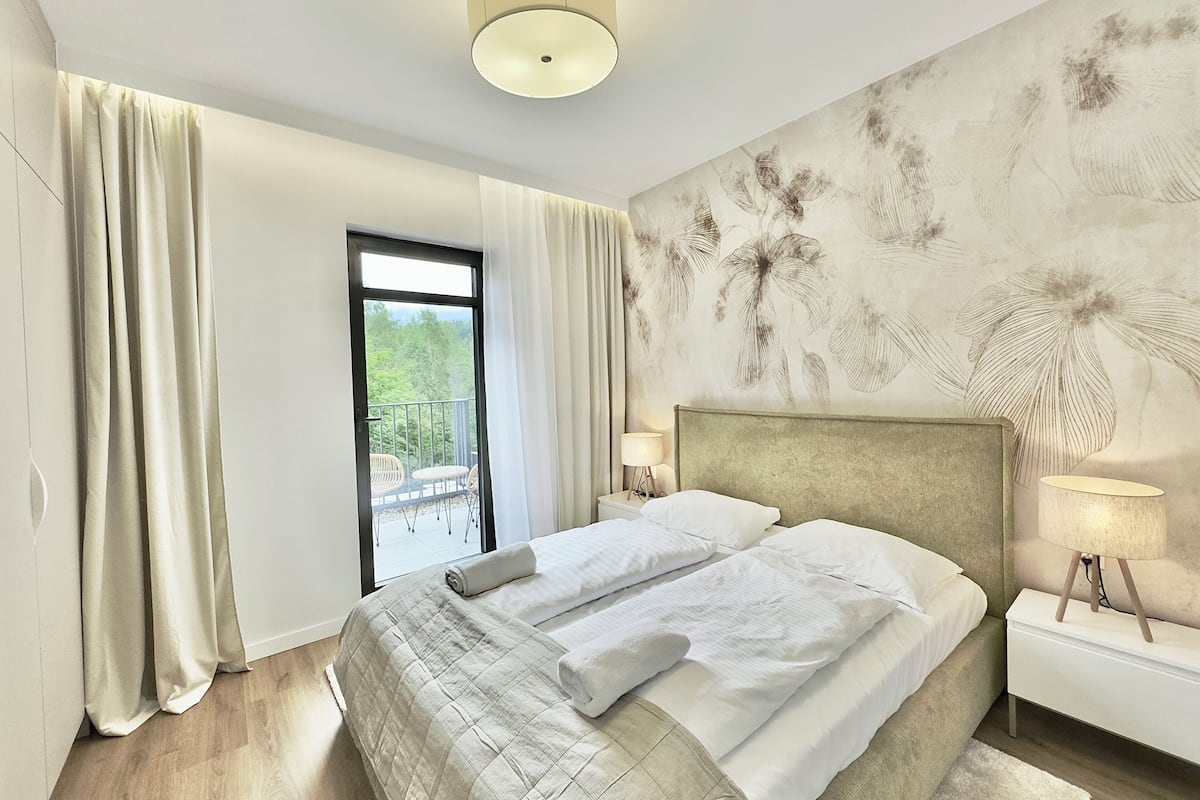 A modern bedroom with a large bed, a view of the outdoors, and a decorative wall.