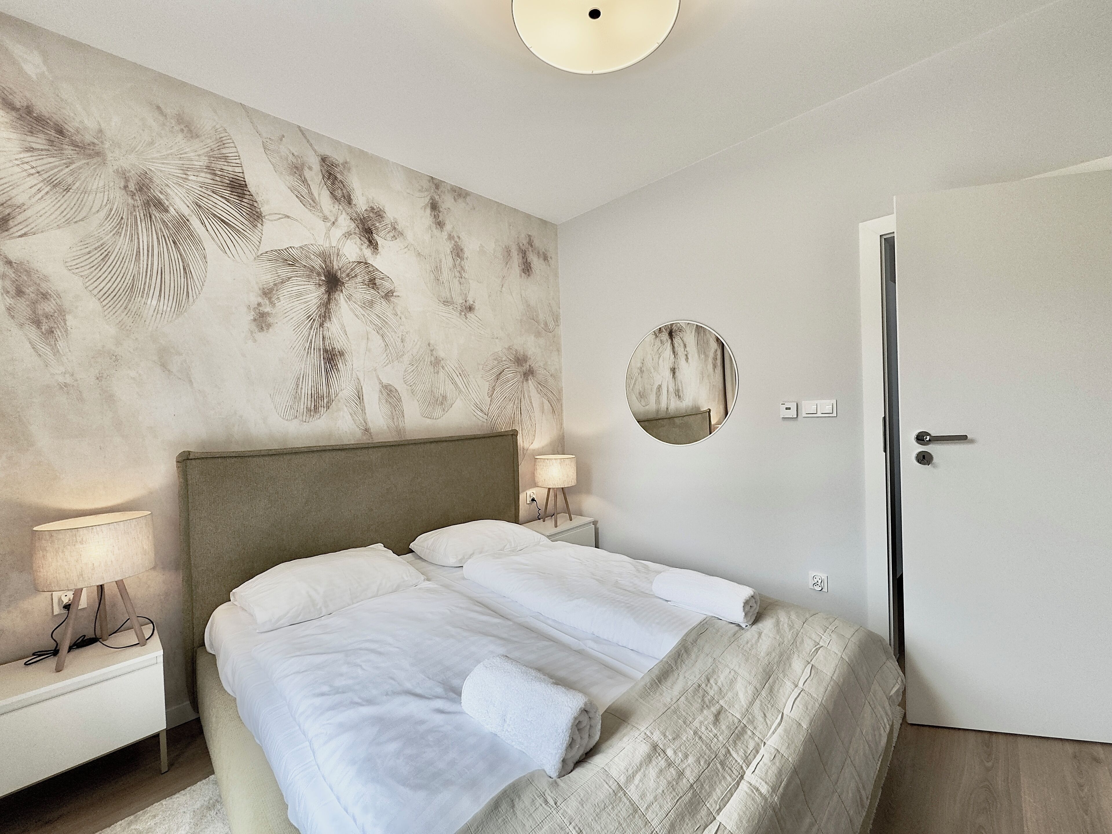 Un dormitorio con una cama grande, una mesita de noche con una lámpara, un espejo en la pared y una puerta.