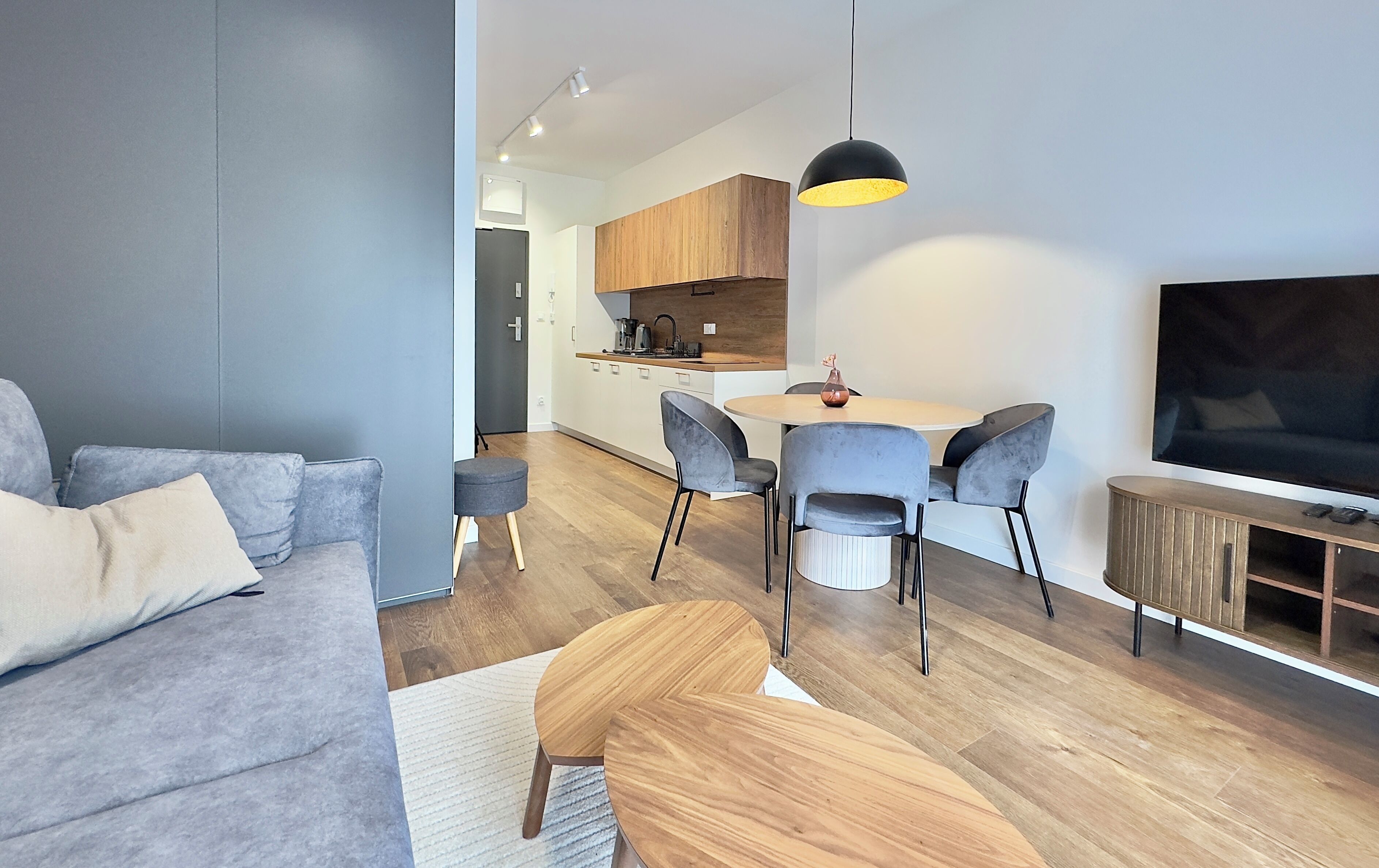 Ein modernes Wohnzimmer mit einem grauen Sofa, einem Holztisch und einem Essbereich mit grauen Stühlen und einem runden Tisch.