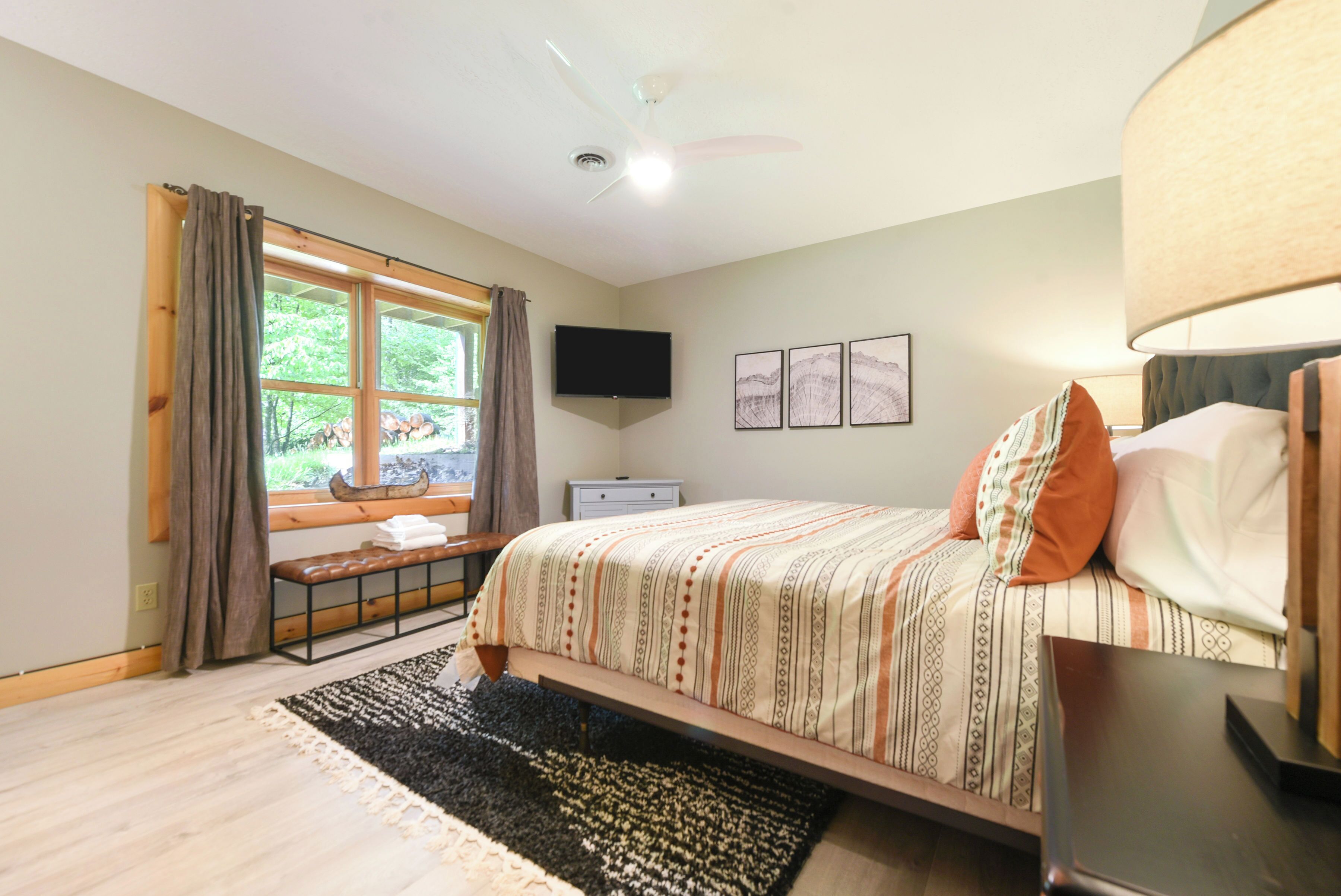 A bedroom with a bed, a bench, a window with curtains, a television, and a nightstand.