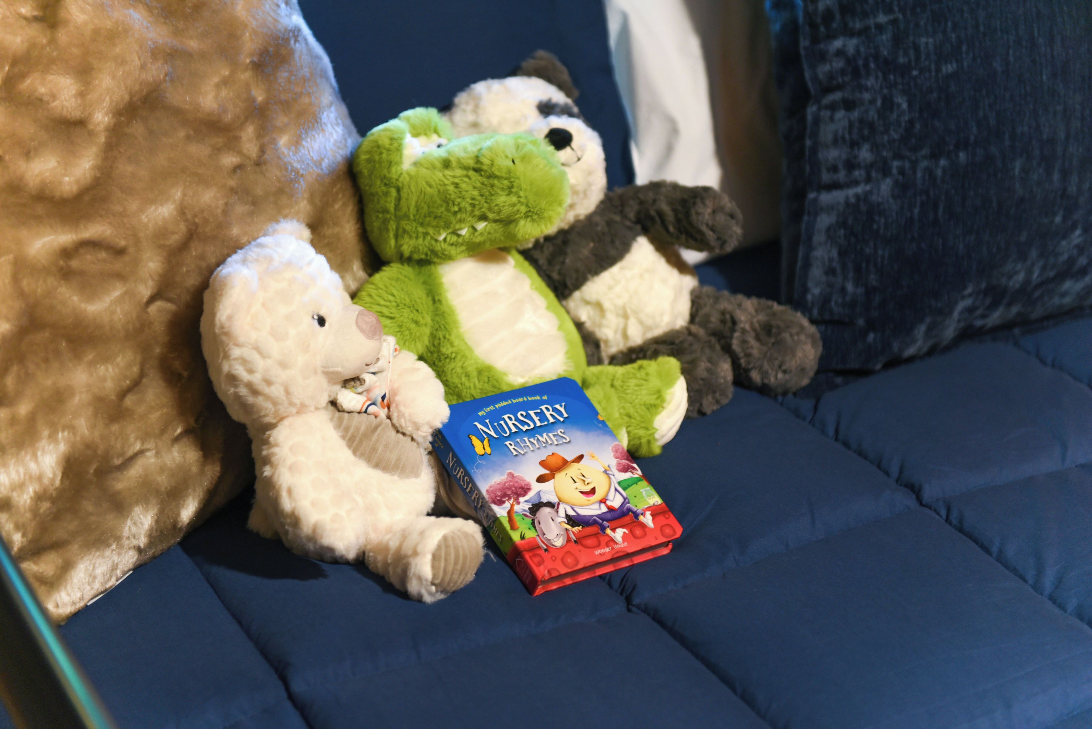 Un canapé bleu avec un livre intitulé « Comptines » et deux peluches.