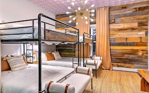 A room with bunk beds, a chandelier, a wooden wall, and a large window.