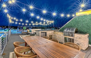 An outdoor deck with a wooden table and wicker chairs, a grill, and a stone wall.