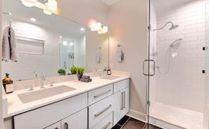 A modern bathroom with two sinks, a large mirror, and a glass-enclosed shower.