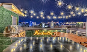 A rooftop bar with a grill, outdoor seating, and a city skyline view.
