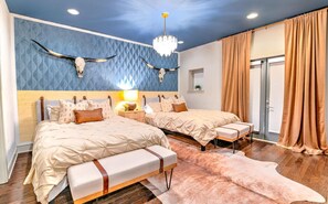 Un dormitorio con dos camas, una araña, una decoración de cráneo de vaca y un ventanal con cortinas.
