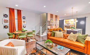 A modern living room with a sofa, coffee table, and chairs, a dining area with a table and chairs, and a staircase leading to an upper level.