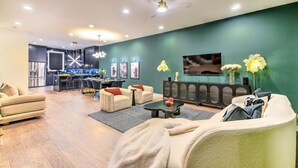 Un salon moderne avec un mur d’accent vert, un téléviseur à écran plat et un coin repas avec une cuisine en arrière-plan.
