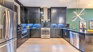 Une cuisine moderne avec des meubles de couleur sombre, des appareils en acier inoxydable et un luminaire original.