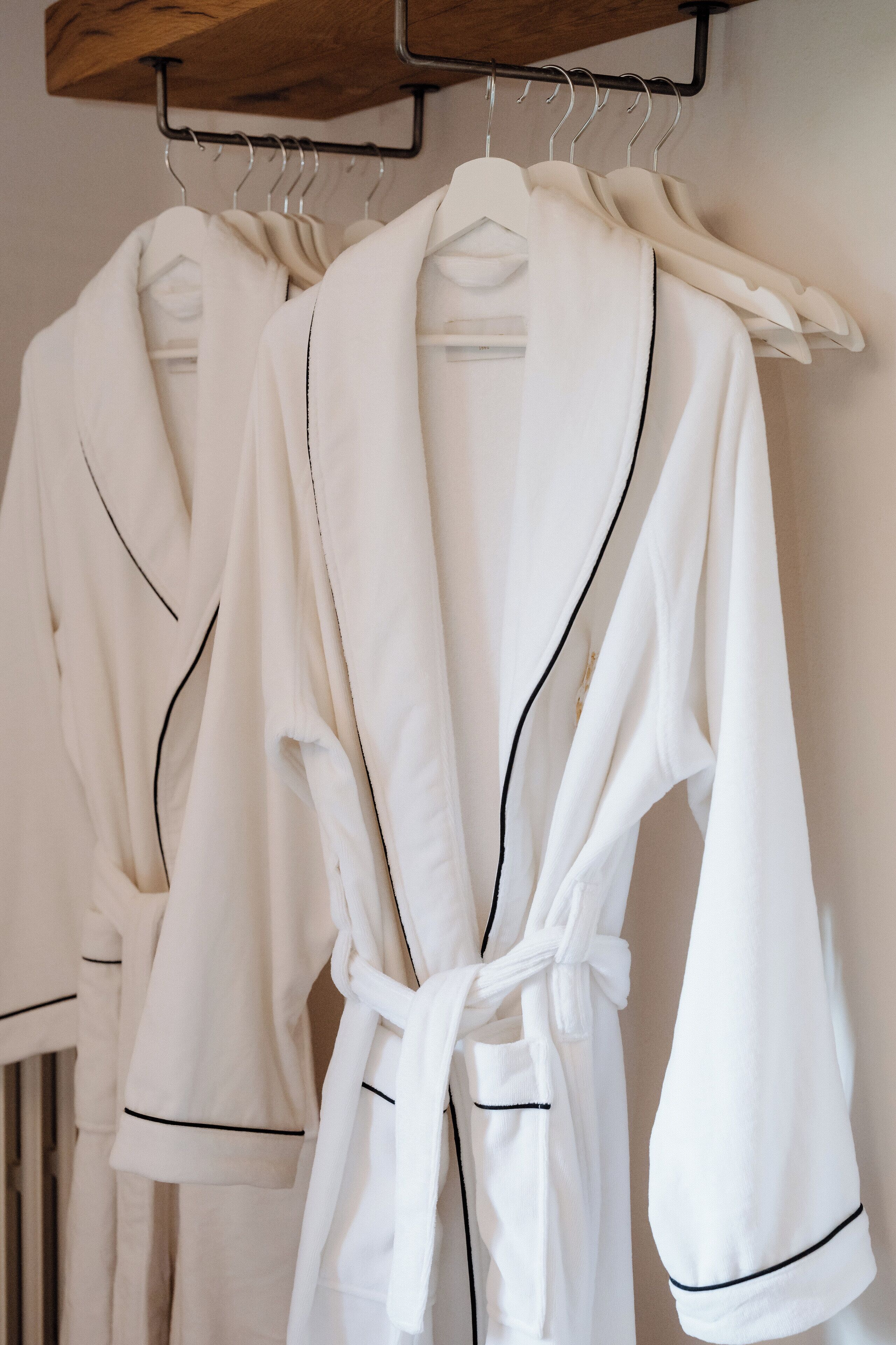 Drie witte badjassen hangen aan een rek.