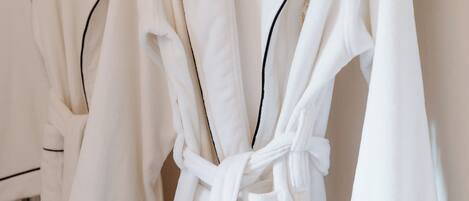 Drie witte badjassen hangen aan een rek.
