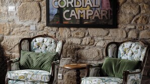 Une pièce avec un mur en pierre, deux fauteuils à motifs floraux et un petit guéridon, ainsi qu’une affiche encadrée de la marque « CORDIAL CAMPARI ».