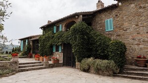 Un bâtiment en pierre doté d’une façade rustique, d’une entrée couverte et de plantes en pot.