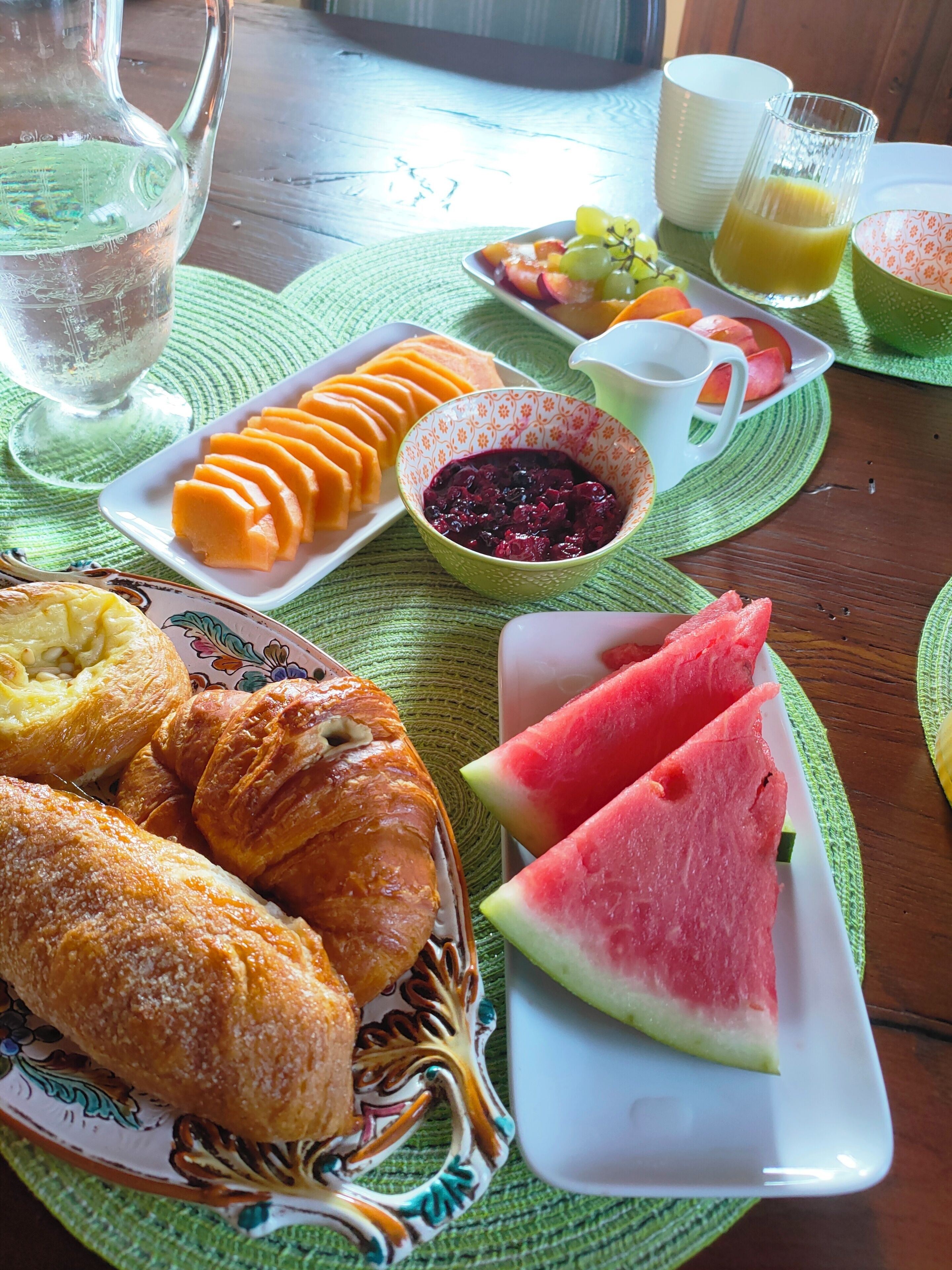 A breakfast table with sliced fruit, pastries, and a jug of juice.