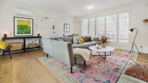 A living room with a gray sofa, a coffee table, a colorful rug, wicker baskets, and a painting on the wall.