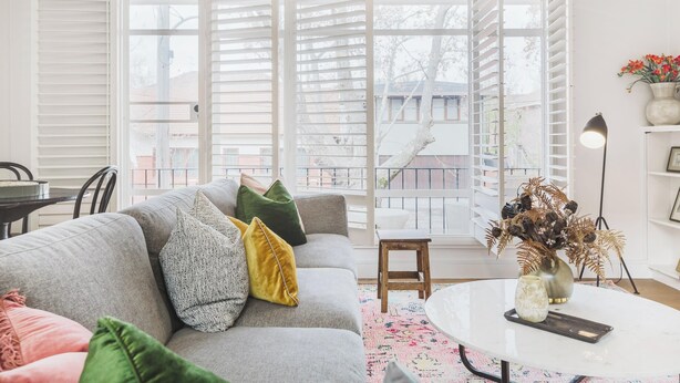 A living room with a grey sofa, a white coffee table, and a view through large windows.