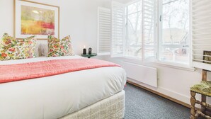 A bedroom with a bed, a window with shutters, a radiator, and a framed picture on the wall.