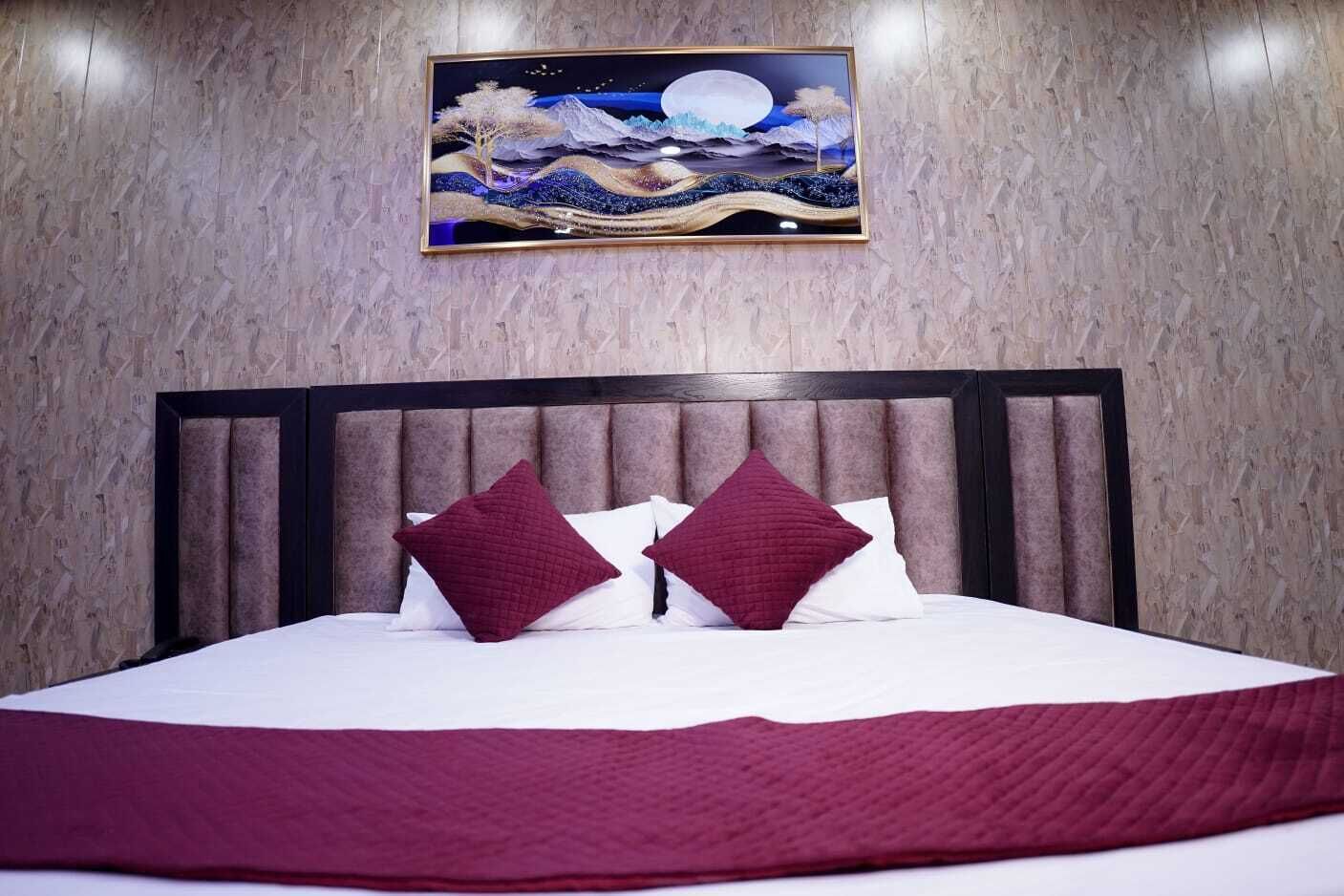 A neatly made bed with a dark headboard, two pillows, and a red blanket.