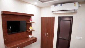 A room with a TV mounted on a wooden wall, a wardrobe, and a refrigerator. - Hotel Amazing House (New Delhi)