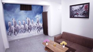 A room with a mural of white horses, a brown sofa, a wooden coffee table with flowers, and a framed painting on the wall. - Hotel Amazing House (New Delhi)