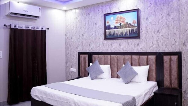 A modern bedroom with a large bed, ceiling fan, air conditioning unit, and a wall-mounted TV. - Hotel Amazing House (New Delhi)