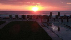 Sonnenuntergang über dem Meer mit Reihen von Stühlen und einem Gebäude im Hintergrund.