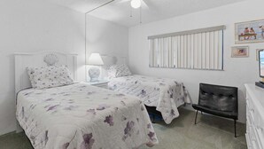 Ein Schlafzimmer mit zwei Betten, einem Deckenventilator, einem Fenster mit Jalousien und einem Sessel.