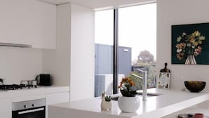 A modern kitchen with white cabinetry, a built-in oven, and a large window providing natural light. - Bright & Stylish Terrace Retreat Richmond (Richmond)