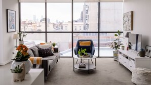 A modern living room with a large window, a sofa, a chair, a coffee table, and a white cabinet. - Bright & Stylish Terrace Retreat Richmond (Richmond)