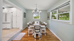 Un coin repas avec une table et des chaises en bois, un lustre et une vue sur l’extérieur par une fenêtre.