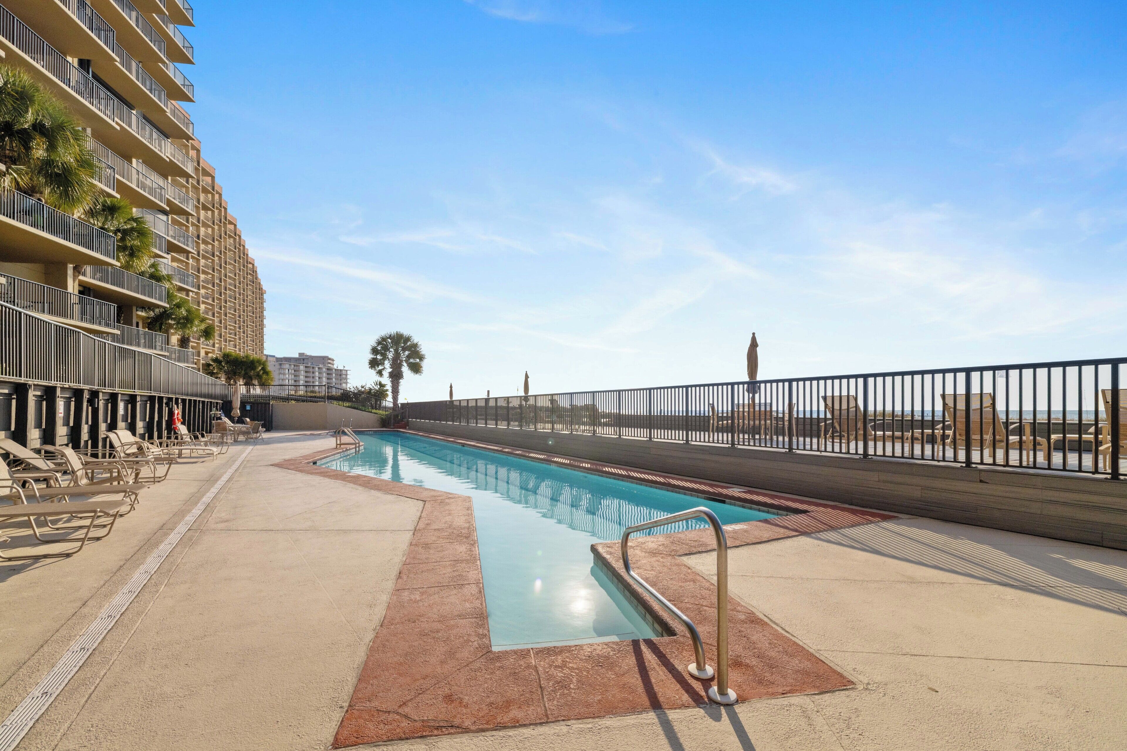 Una piscina con sillas de descanso, una valla y un edificio con balcones.