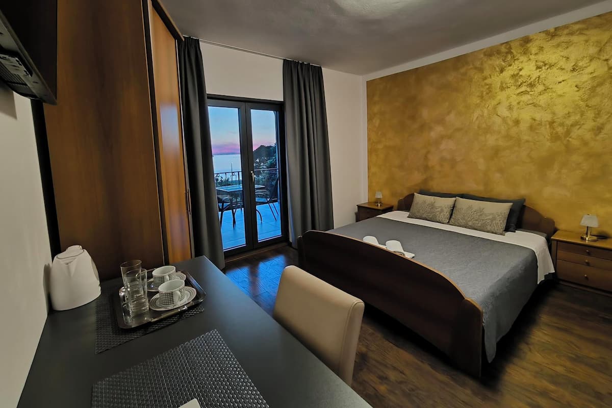 Een hotelkamer met een bed, een bureau met een dienblad glazen en bekers, uitzicht op de stad door een groot raam, en een gestructureerde muur.