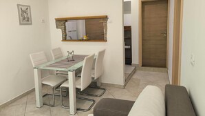 A compact living space with a dining table, chairs, a sofa, a kitchen area with a refrigerator, and a wooden door. - Rooms and Apartment Matika (Rovinj)