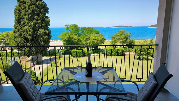A balcony with a table and two chairs, overlooking a coastal view with trees and the sea. - Rooms and Apartment Matika (Rovinj)