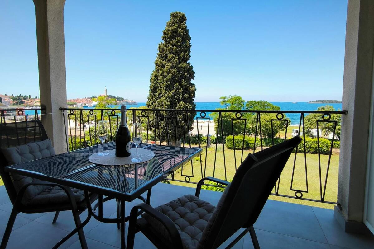 Een balkon met tafel en stoelen, met uitzicht op de kust onder een heldere lucht.