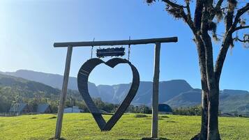A heart-shaped metal structure with a sign, a tree, and a mountainous landscape in the background.