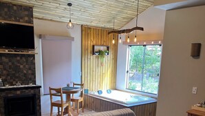 A room with a bed, a massage table, a small table with chairs, a fireplace, and a window with a view of greenery. - Pousada Recanto dos Canyons (Praia Grande)