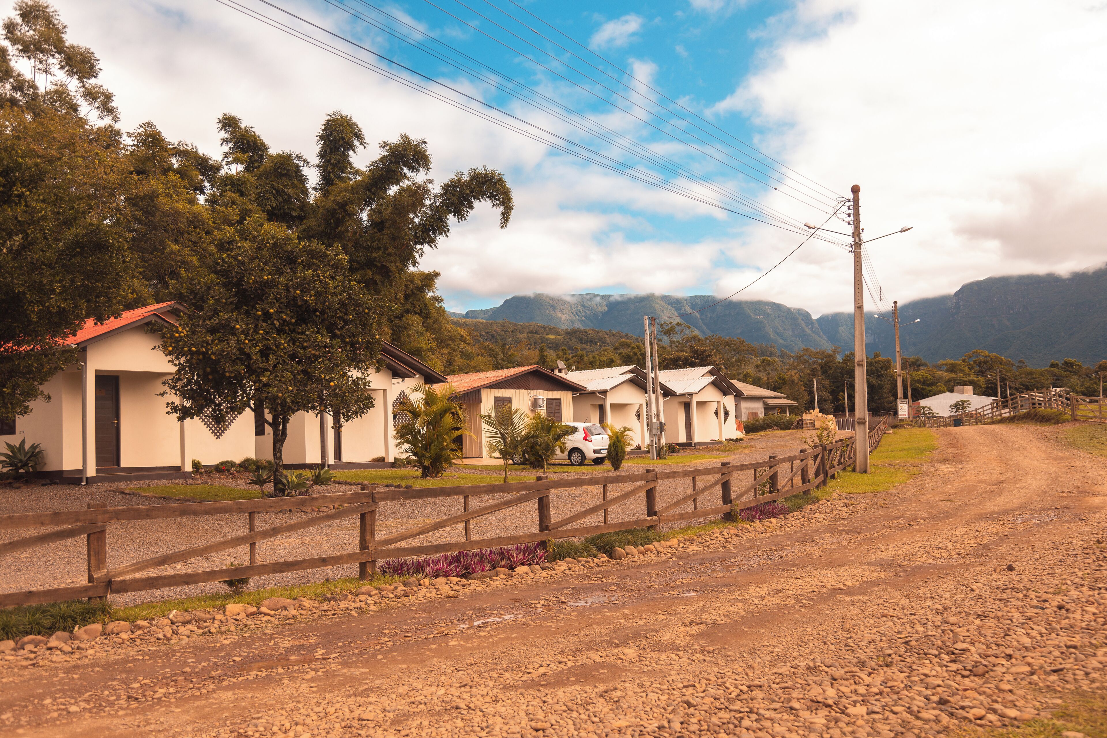 A row of single-story houses with a gravel driveway, surrounded by greenery and mountains in the background.