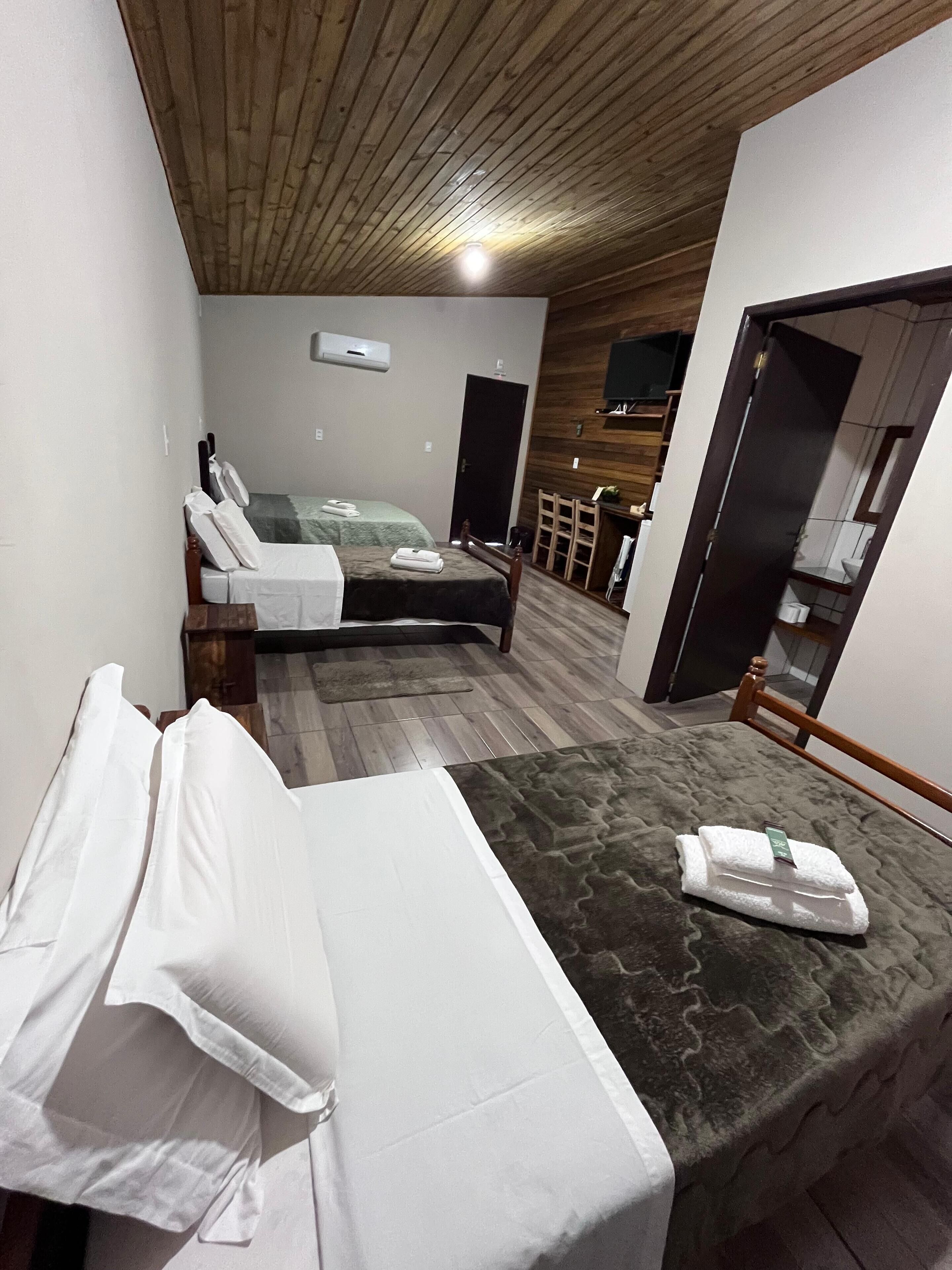 Un dormitorio con cama, sofá, techo de madera y televisor en la pared.